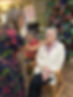 Woman in floral dress helps older woman in a chair near a decorated Christmas tree