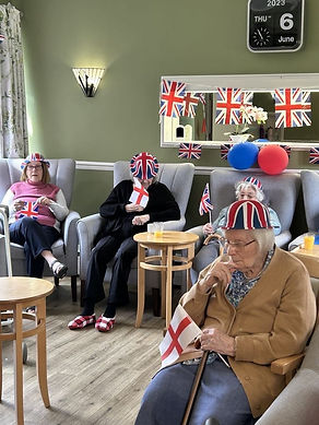 Elderly women in chairs wear Union Jack hats, holding English flags