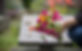 Close-up of a colorful bouquet of pink, orange, yellow, and white flowers placed at a gravesite, with a softly blurred background