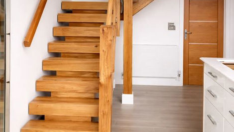 Modern interior with wooden stairs leading up, light wood flooring, and white walls