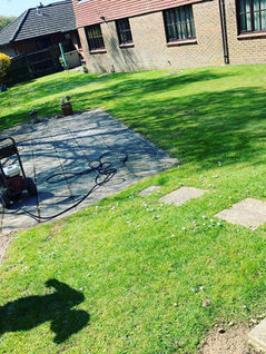A sunlit backyard with a freshly mowed lawn, stone patio, and two-story brick building
