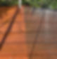 A wooden deck showing a contrast between cleaned and uncleaned areas, with one side appearing bright and new while the other side is dull and weathered