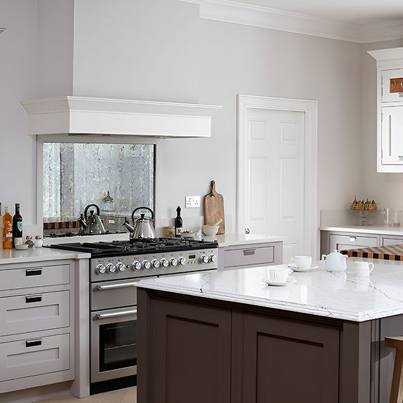 Marble-topped kitchen island beside stainless range cooker and shaker cabinetry.