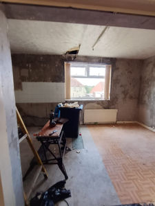 Room undergoing renovation with bare plaster walls, exposed ceiling joists, and a window in the background