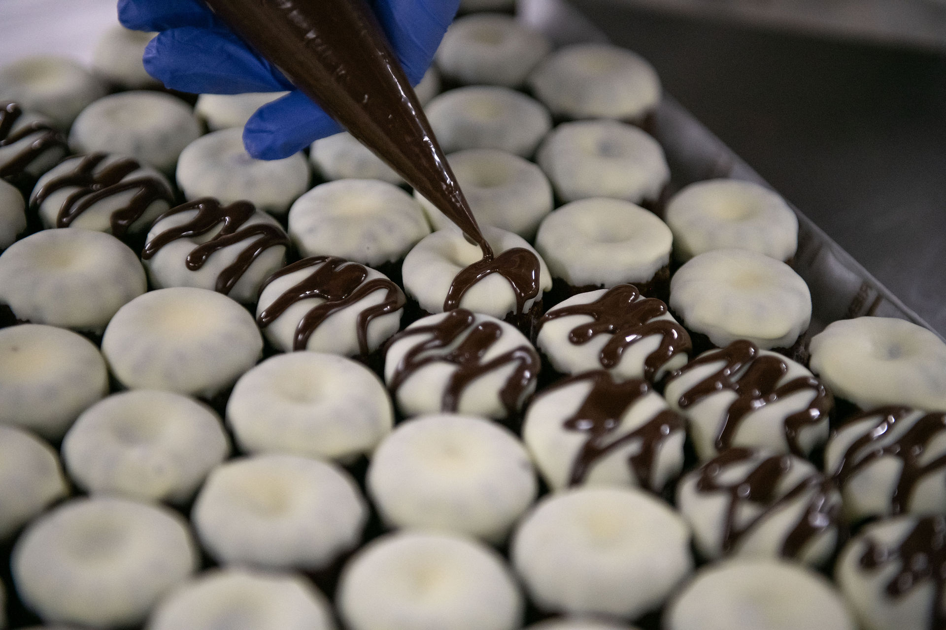 ホワイトチョコがかかったカヌレに、茶色いチョコをパティシエがプロの手つきでかけている