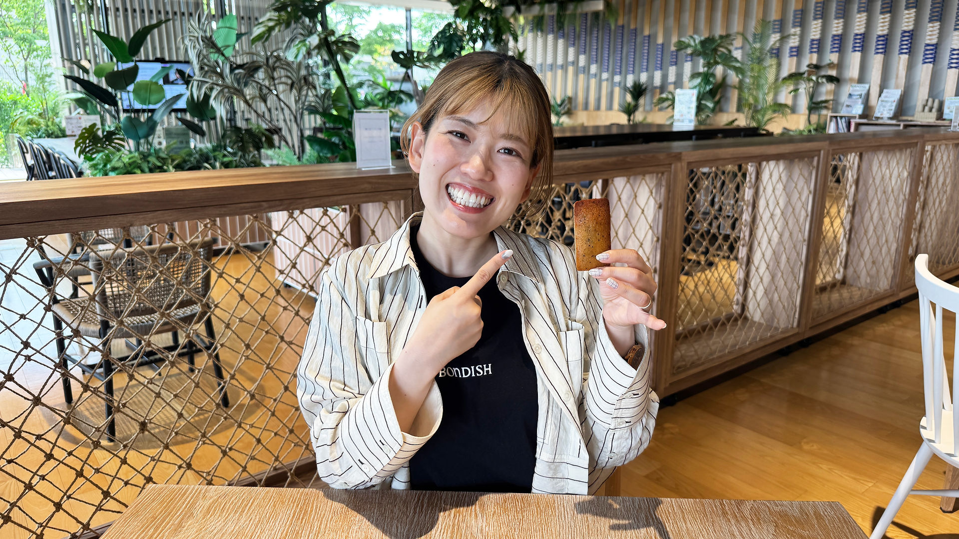 笑顔の女性がコーヒー味のフィナンシェをもって指さしている。
