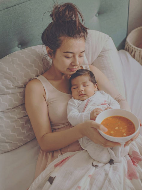 Mutter im Wochenbett mit Baby genießt fertige Mahlzeit zu Hause