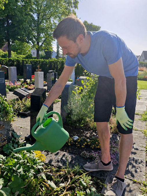 Mann gießt Pflanzen auf einem Grab auf dem Friedhof.