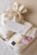 Cremefarbener Satinbeutel, Stillponcho und elegante Geschenkkarte als liebevoll arrangiertes Geschenkset für Mütter.
