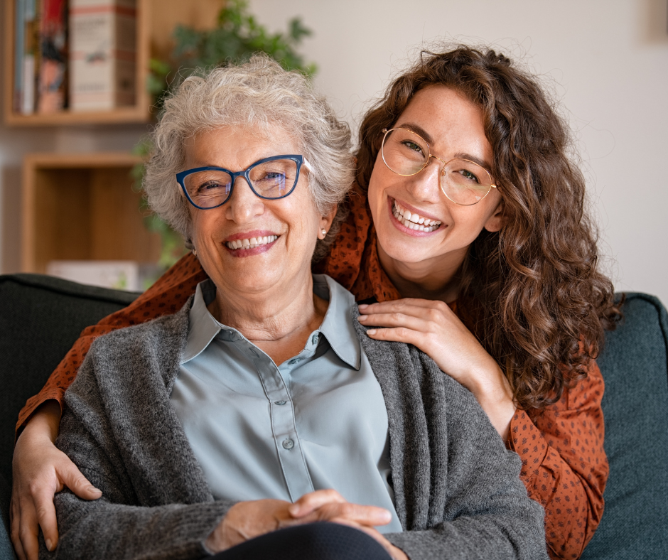 Adult daughter smiling and hugging her elderly mother at home, representing family bonds and home care support in South Gloucestershire.