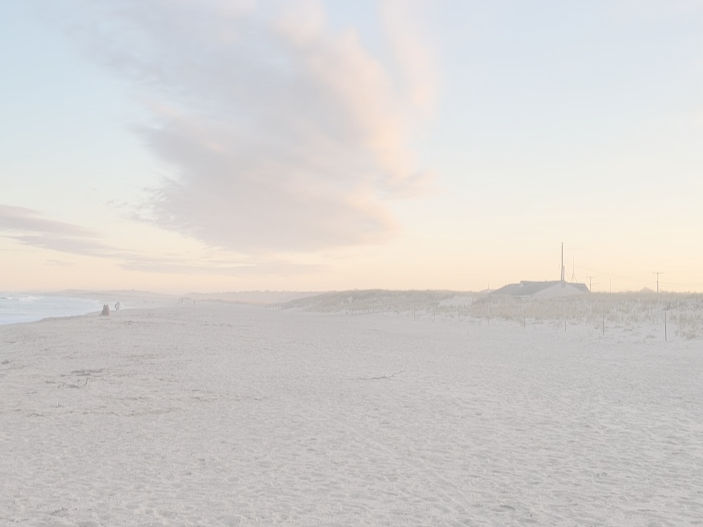 Sunset and clouds in sky looking down a beach with tiny distant figures on the shoreline