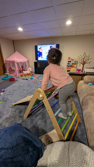Toddler engaging in gross motor play on Pikler triangle in an organized basement playroom designed for work-from-home moms