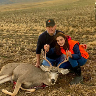 Dan with his daughters Maddie and Mary with a dead deer they hunted and a sunset behind them.