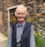 A dog and cat sitter living in Devon, wearing a navy ble checked shirt and a navy body warmer standing in front of an old brick wall