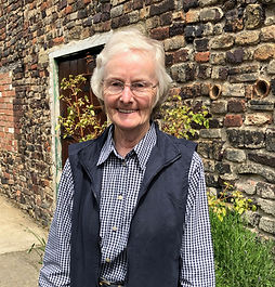A dog and cat sitter living in Devon, wearing a navy ble checked shirt and a navy body warmer standing in front of an old brick wall