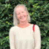 Dog and pet sitter living in Cornwall standing, wearing a cream jumper with a red shoulder bag and a green hedge behind