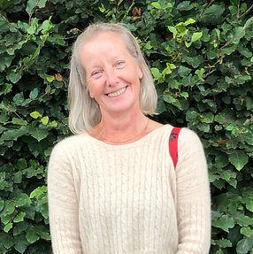 Dog and pet sitter living in Cornwall standing, wearing a cream jumper with a red shoulder bag and a green hedge behind