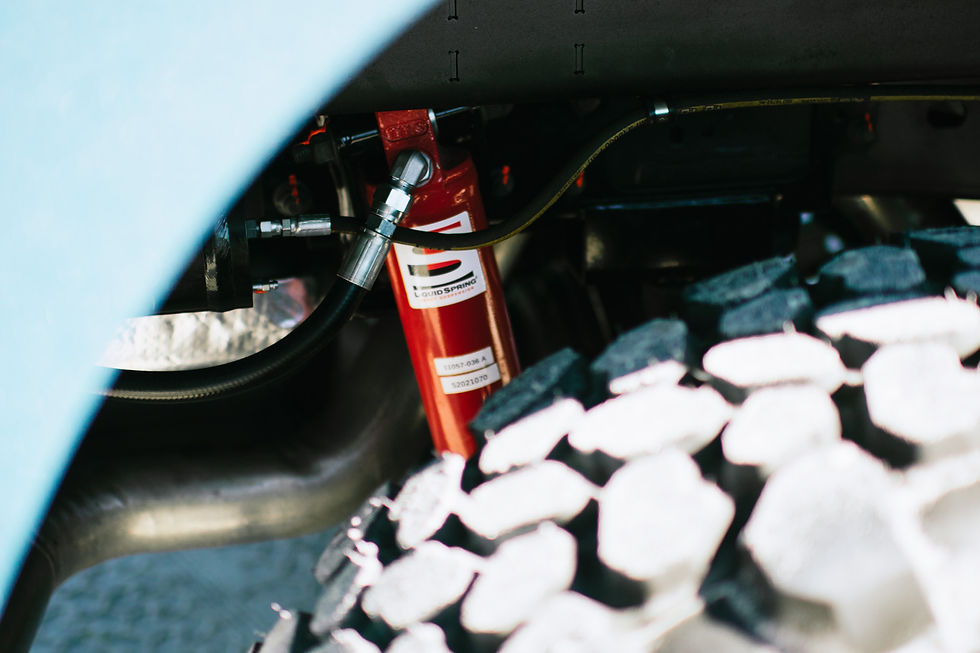 Close-up of a red Liquid Spring suspension unit behind the off-road tire of a 27North TR27 expedition truck