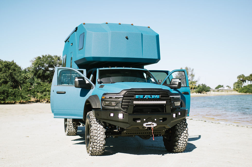 Front view of a blue 27North TR27 expedition habitat on a Ram 5500 chassis with off-road bumper and winch on a beach