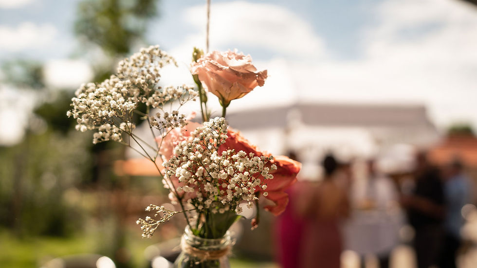 individuelle Blumendekoration: Blumen hängen in einer Vase an einem Seil, im Hintergrund eine Hochzeitsgesellschaft