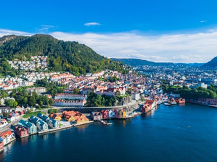 Aerial view of a colorful coastal town with houses, hills, and blue water under a clear blue sky. Vibrant and serene scenery.