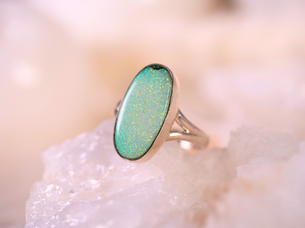 Sterling-silver ring with a glowing oval green opal and vivid blue-gold play-of-color. Meaning: creativity, inspiration, joy.