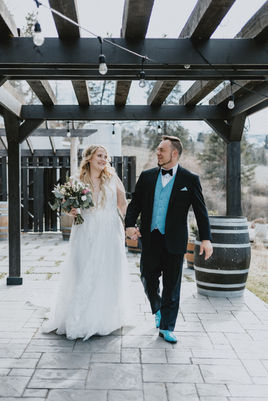 A smiling newlywed couple walking hand in hand toward the camera as they smile at one another at Summerhill Pyramid Winery, Kelowna.