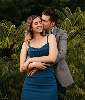 A man embracing a woman from behind kisses her on the cheek as she smiles.
