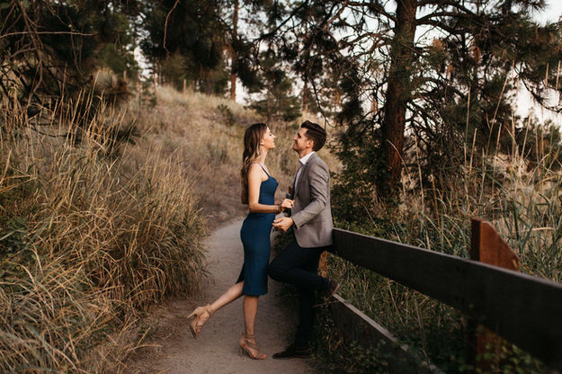A wide angle of a woman smiling and leaning toward a man who is resting on a wooden fence.