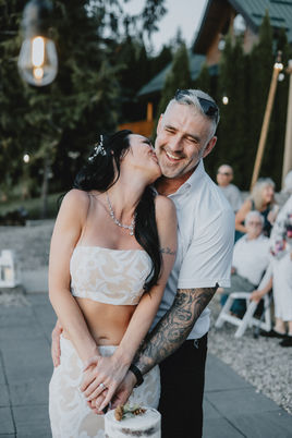 A newlywed bride kissing her smiling groom on the cheek as they cut their wedding cake together.