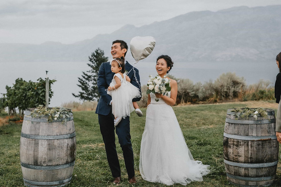 A bride and groom laughing with their young daughter at their wedding ceremony