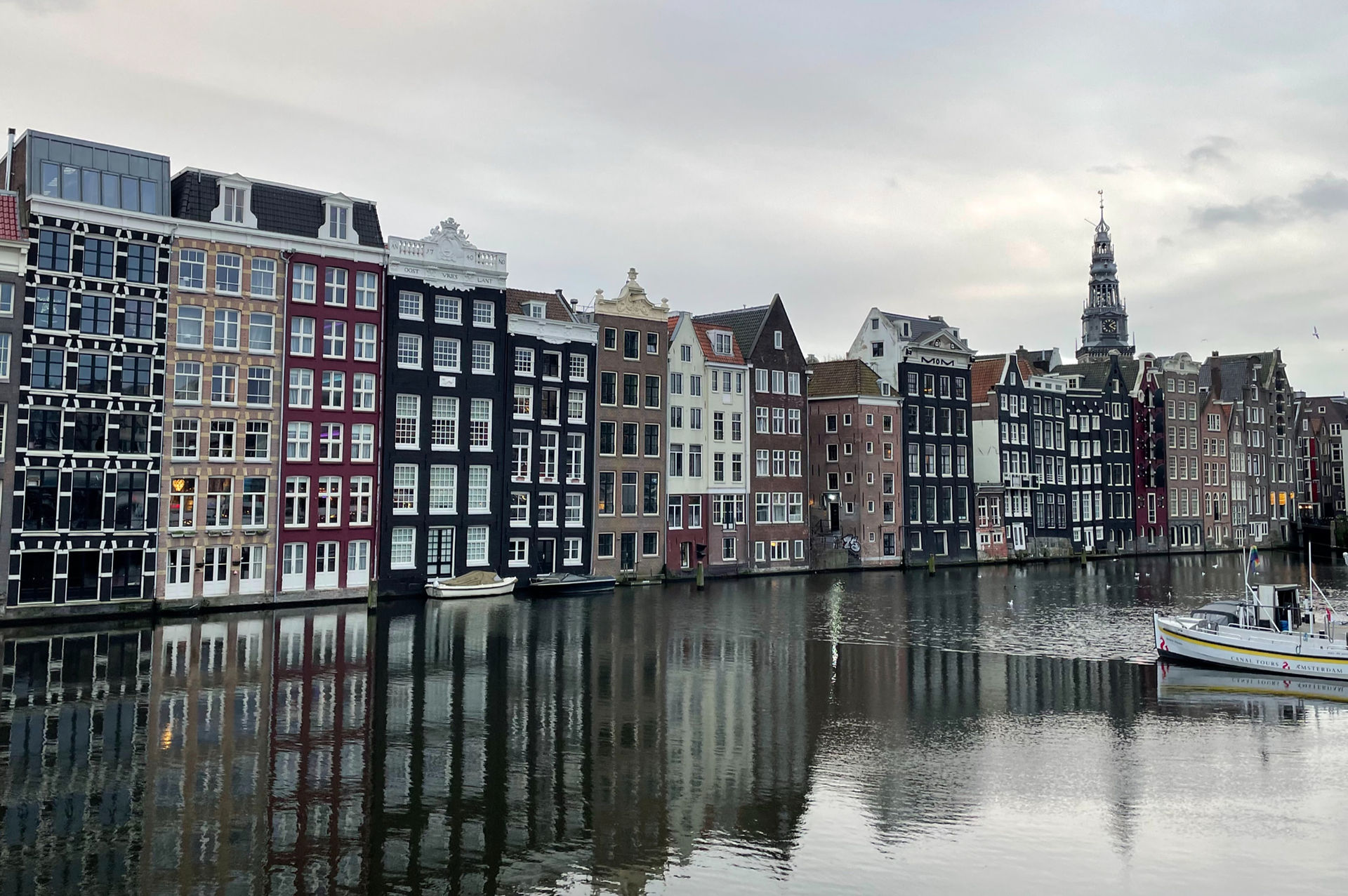 Amsterdam canal houses reflecting in the water during overcast weather conditions.