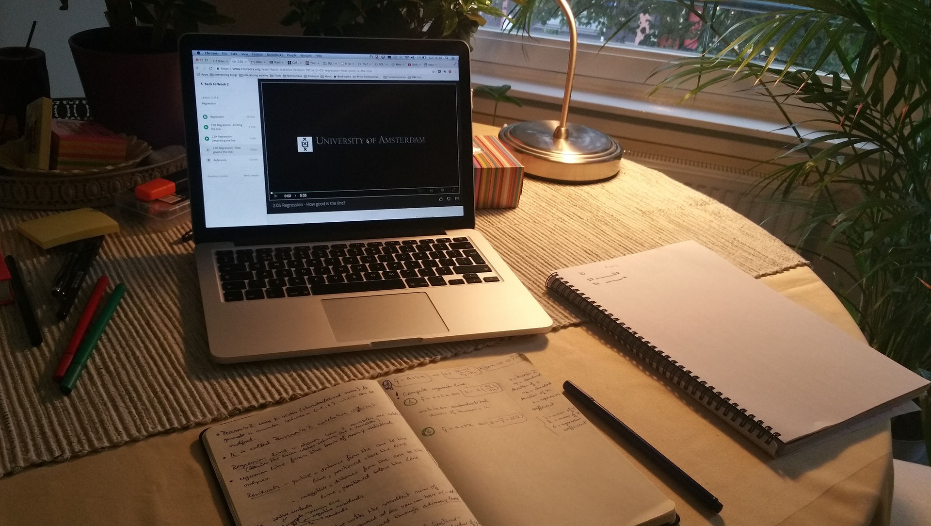 Laptop with video playing and open notebooks on a desk, studying environment.
