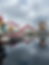 Ferris wheel with a Mickey Mouse face and a roller coaster reflected in a calm lake at Pixar Pier, under a cloudy sky.