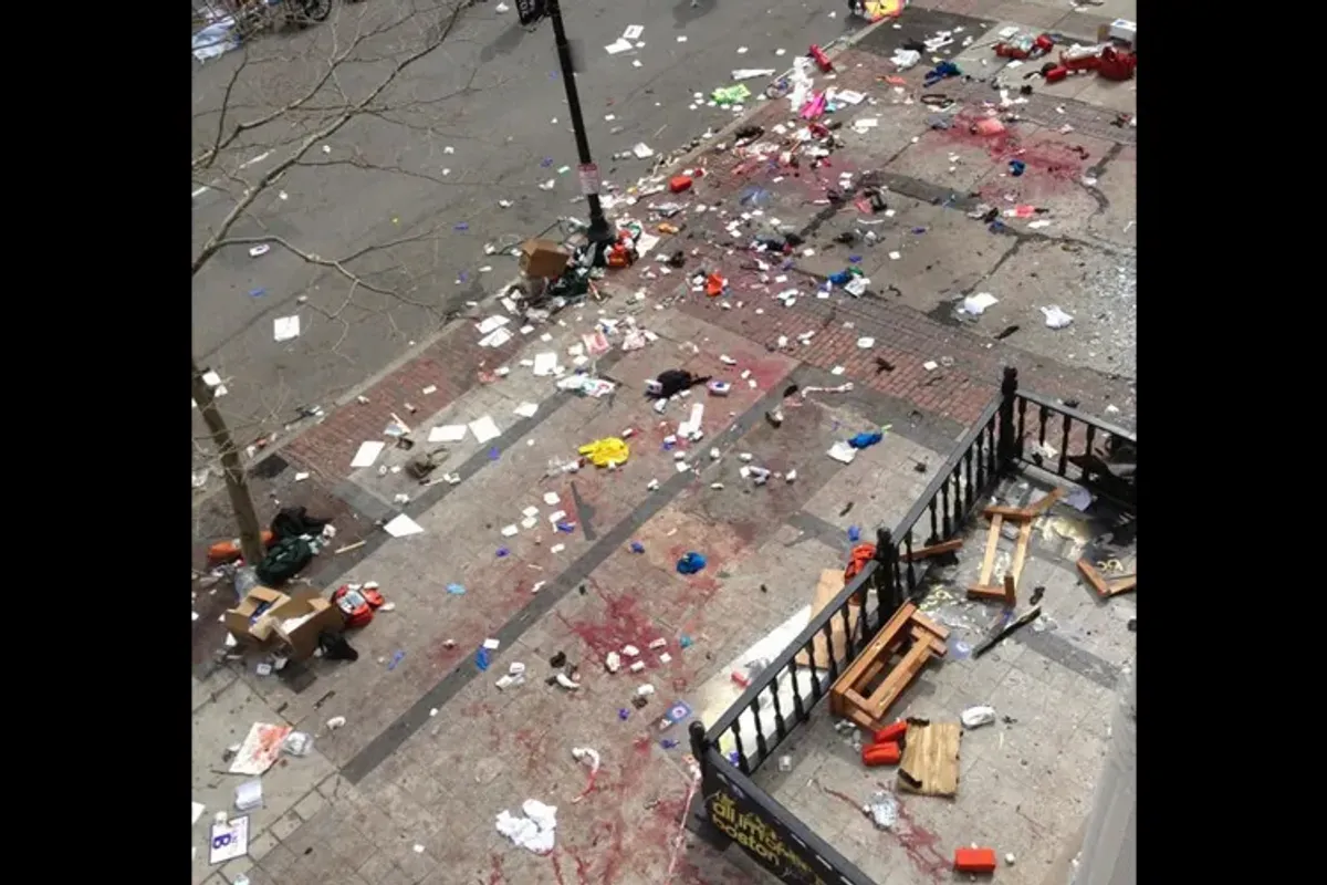 Ariel view of sidewalk littered with debris. A viewing platform littered with broken wooden furniture. Large blood stains on sidewalk and viewing platform.