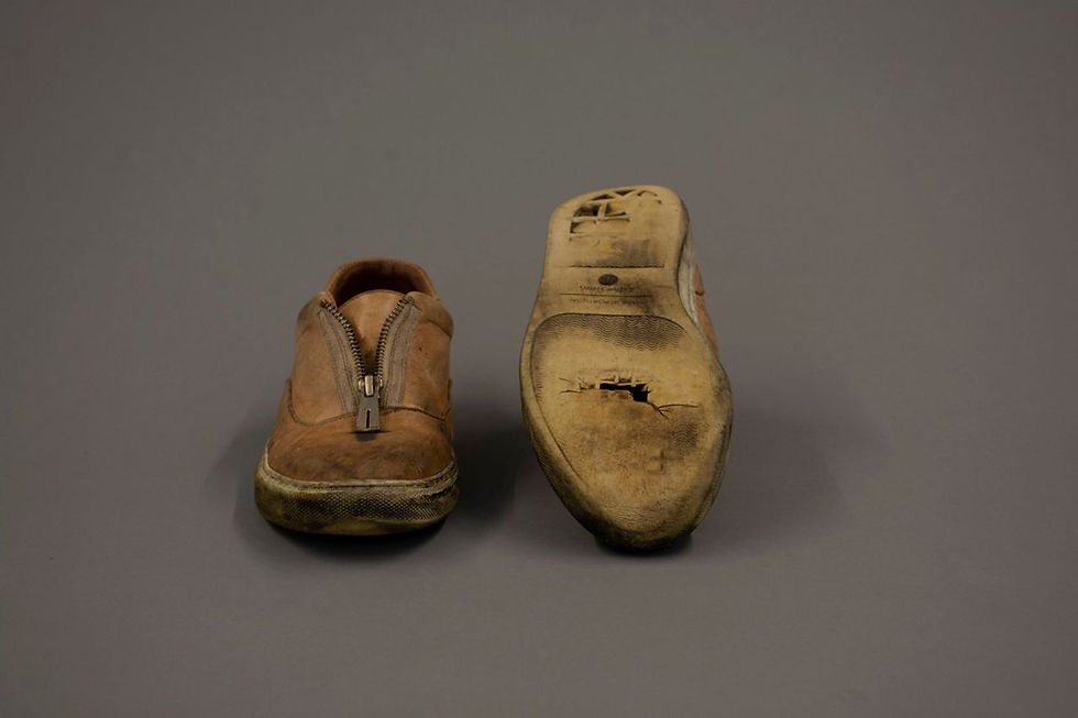 Pair of worn brown shoes, one right-side up, scuffed with a zipper down the center and the other upside-down with a hole in the sole and worn-down heel.