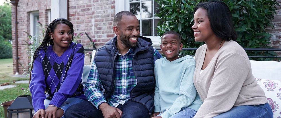 An African American family, daughter, dad, son and mom, all happy outside.