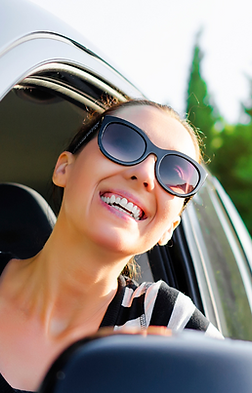 Femme heureuse conduisant une voiture, portant des lunettes de soleil et souriant par la fenêtre