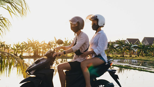 Couple riding a motorbike near rice fields in Bali, both wearing helmets and masks
