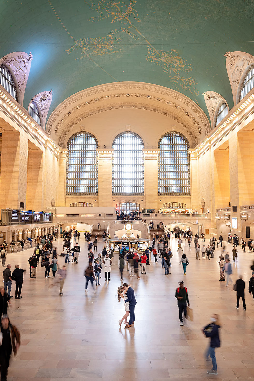 Romantic engagement photo of a couple sharing an intimate moment inside Grand Central Station in New York City, surrounded by crowds. 