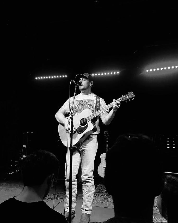 Jimmy Fitch performing live at Richmond Music Hall in Richmond, Virginia with an acoustic guitar and microphone in a black-and-white concert photo.