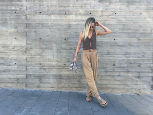a woman in a brown top and tan pants is standing in front of a concrete wall