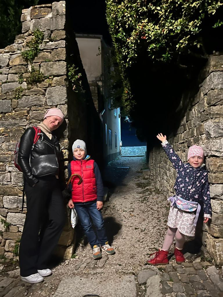 Mother with two children standing in a stone alley at night, smiling and pointing toward the path ahead.