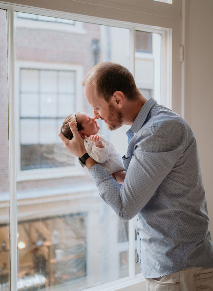 A tender moment between daddy and baby, their noses gently touching, eyes closed in pure love. The warm sunlight streams through the window, casting a soft glow over this precious bonding moment, filled with joy and connection.
