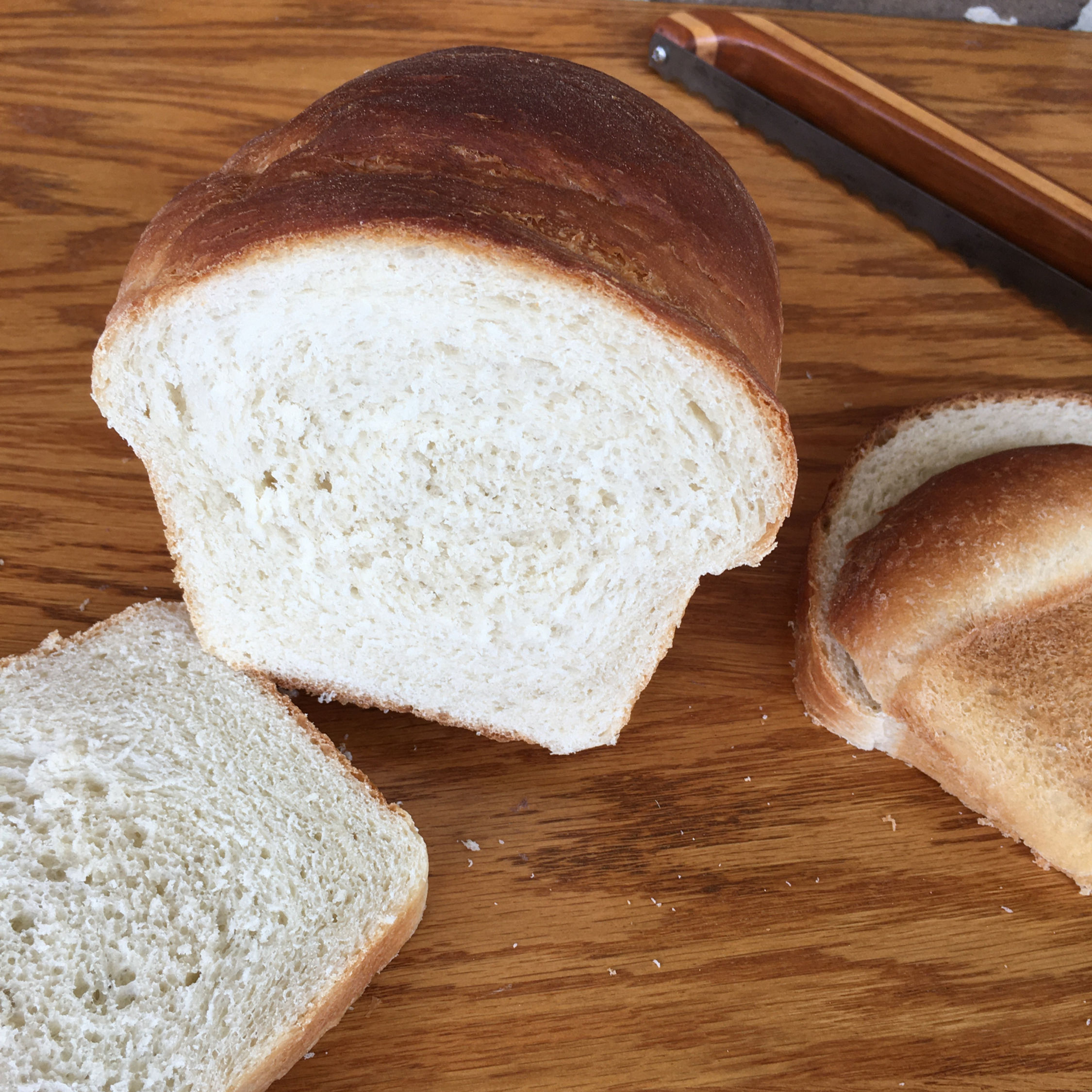 Loaf of white bread, sliced, on a wooden board.
