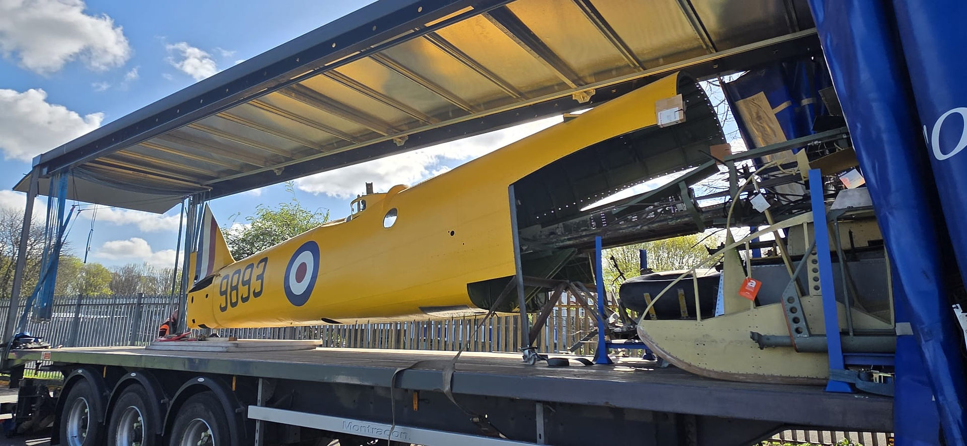 a yellow aircraft fuselage with number 9893 being unloaded from a lorry trailer. 