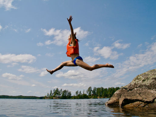woman in life jacket jumping enthusiastically into lake