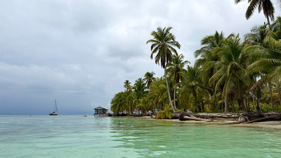 Calm tropical beach with palm trees, a small hut and sailboat under a cloudy sky, clear turquoise water in the foreground