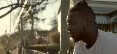 Young Black man with dreadlocks, looking thoughtfully to the right.