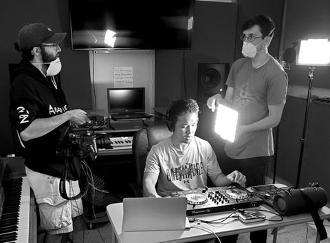 Three people in masks filming a DJ in a studio